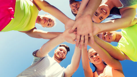 Gruppe fröhlicher junger Menschen berührt sich an den Händen